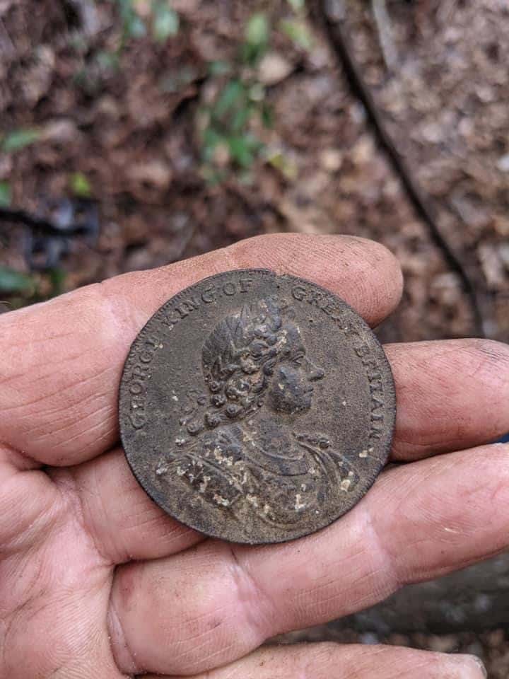 Indian Peace Medal Uncovered in North Carolina held in dirty hand with leaves and dirt in background