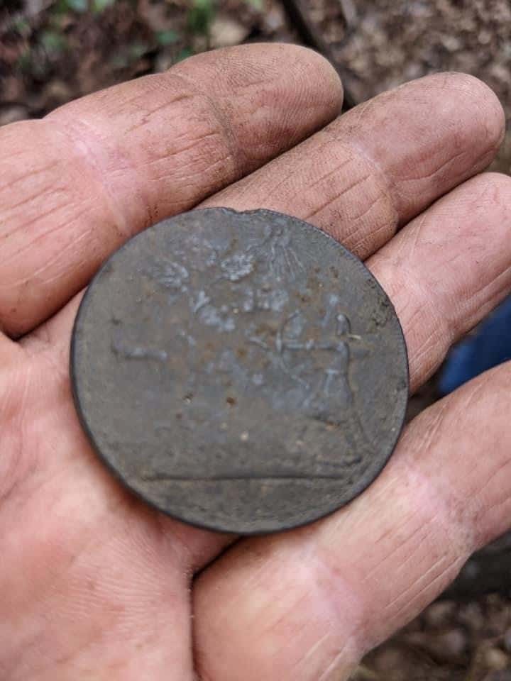Reverse of Indian Peace Medal Uncovered in North Carolina held in dirty hand with leaves and dirt in background