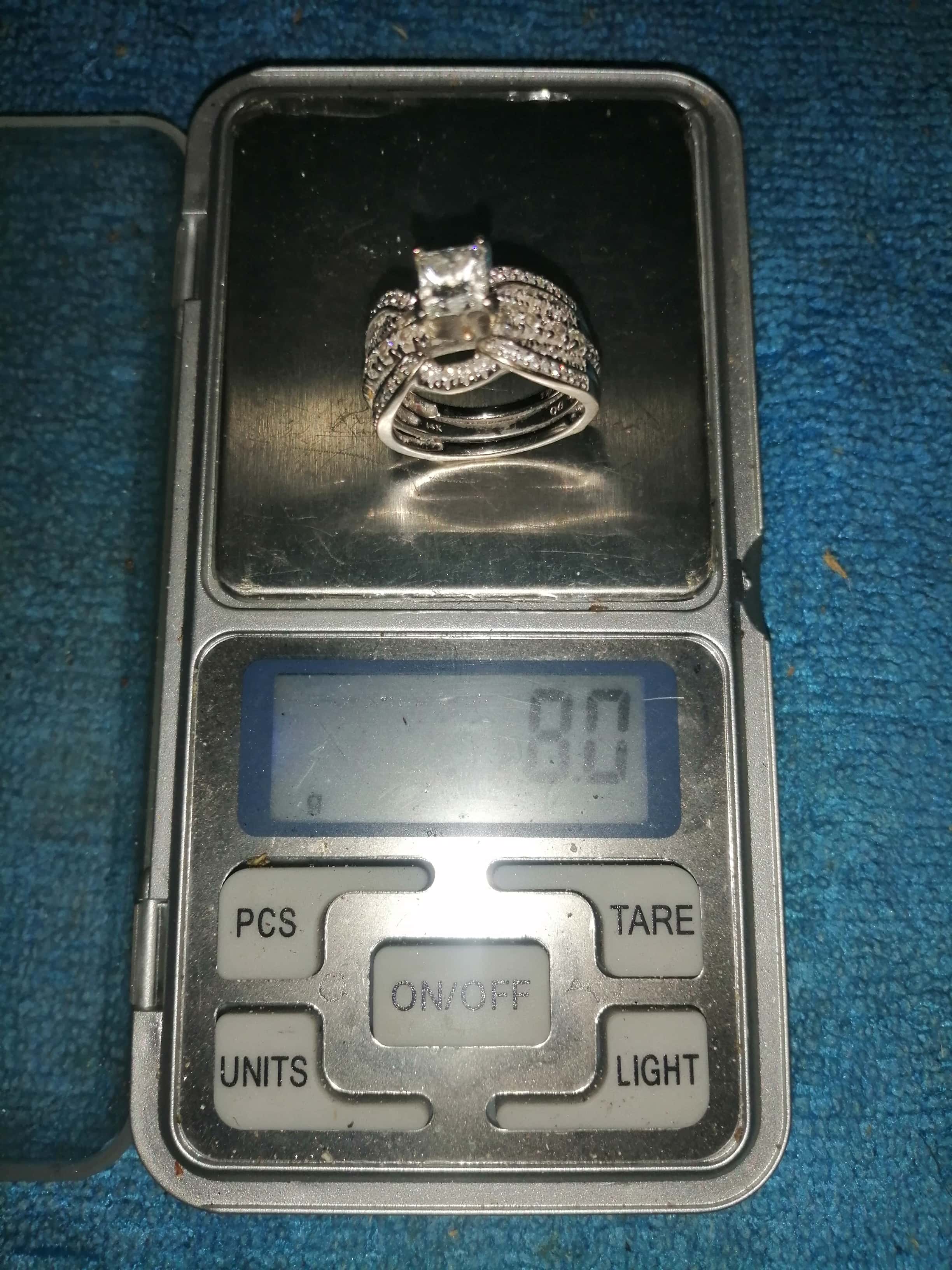 Platinum and Diamond Ring Resting on LCD Scale with 8.0g Shown on Sceen and Buttons Beneath on Blue Background