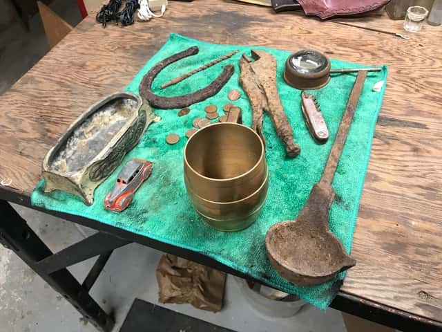 Brass Cup and Other Finds Arranged on a Green Towel On an Old Wooden Table