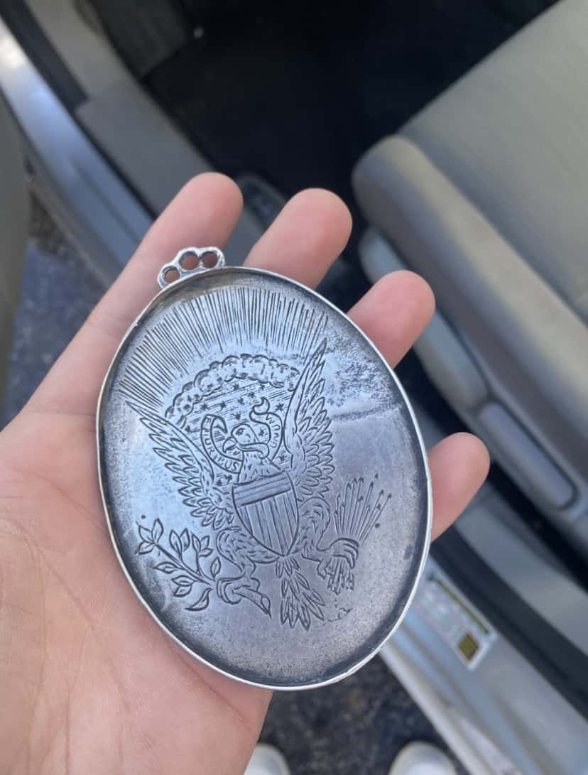 Image of Back of Peace Metal Held In Hand with Blue and Gray Seats Blurred in Background