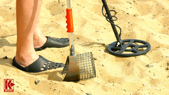 A detectorist using a sand scoop and metal detector on the beach.